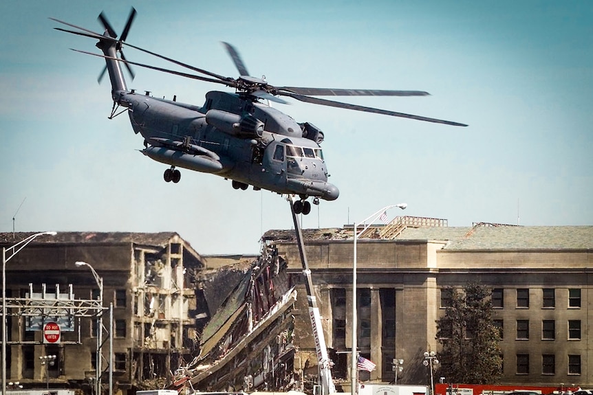 A military chopper flies over the Pentagon, with part of the wall caved in