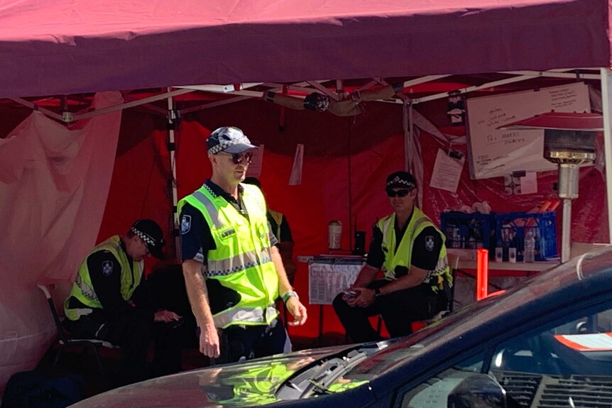 Three police officers check vehicles while inside a big red tent.