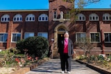 Josephite Sister Margaret Ng stands in front of brick religious building and garden.