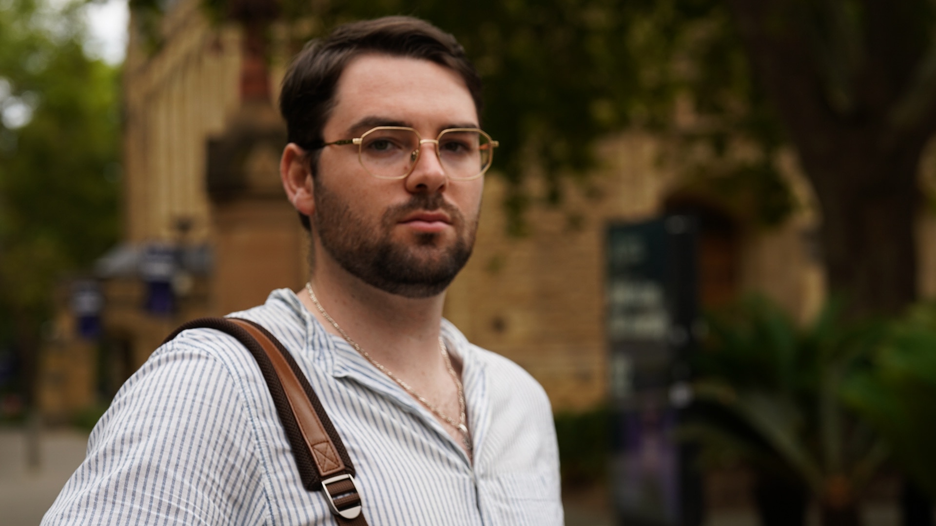 Benjamin Lianio veste uma camisa de gola listrada e uma alça de bolsa marrom no ombro.
