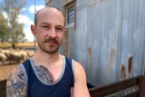 Male shearer with tattoos standing in front of shed