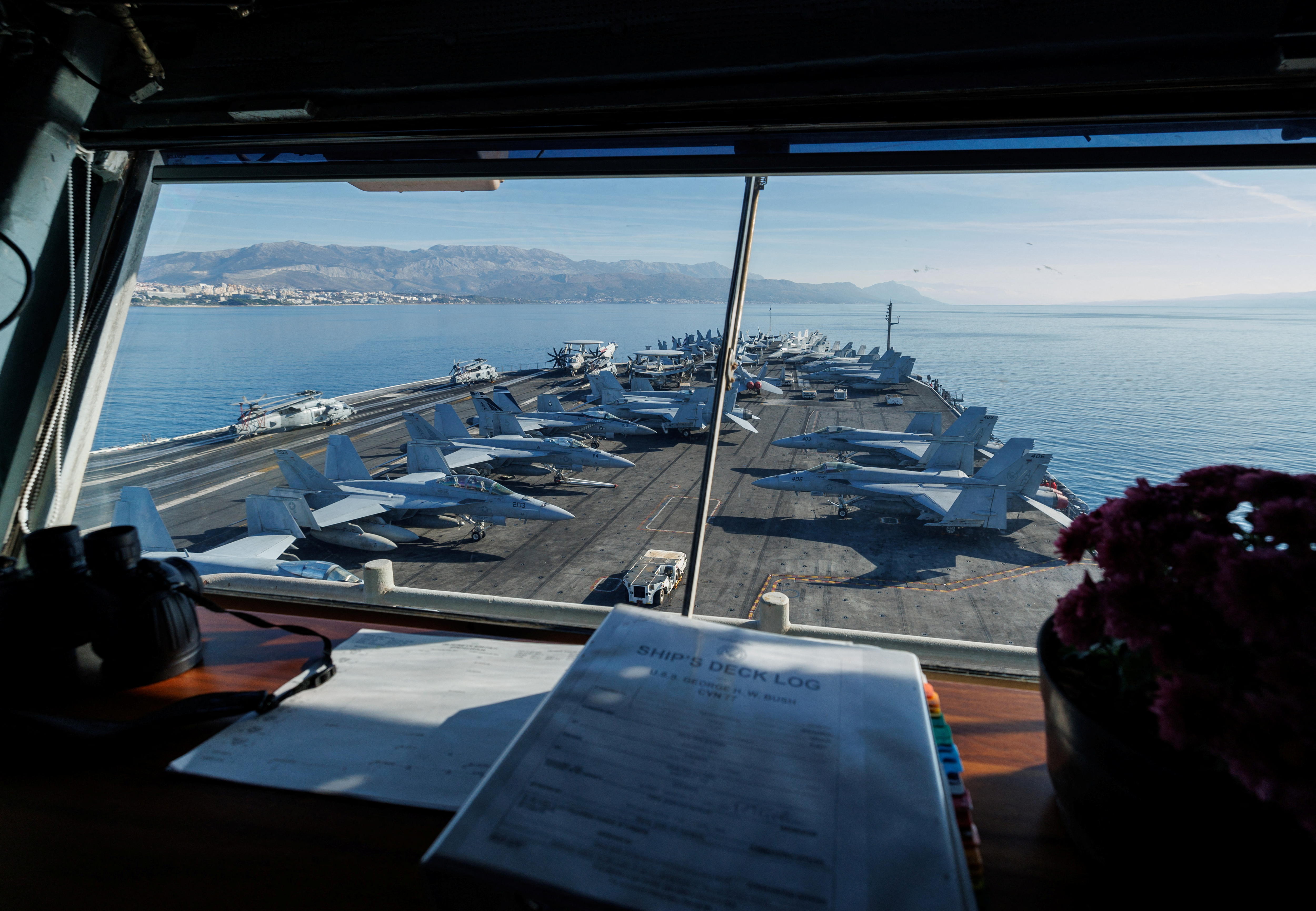 a view through the front window of a ship carrying jet planes on the deck 