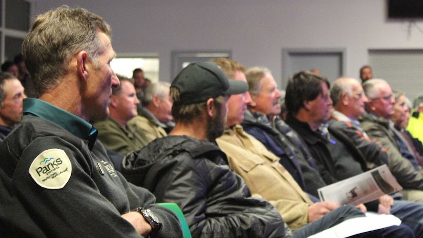 Residents and authorities sit in a row of chairs at a forum.