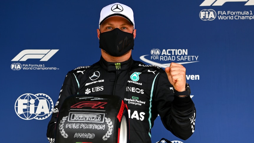 A mask-wearing F1 driver holds a trophy after taking pole position before a race.