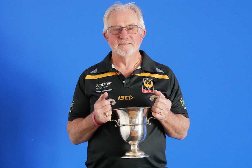Man with grey hair and glasses holds a silver coloured trophy cup in two hands 