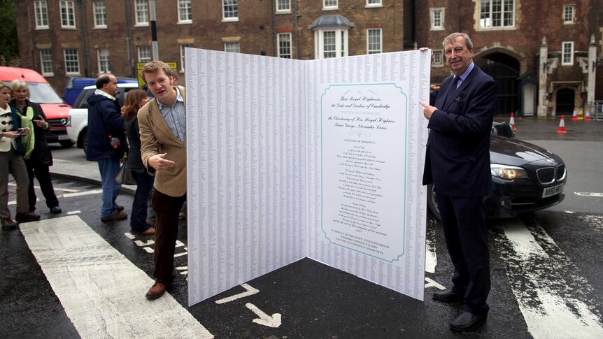 A giant Christening card for Prince George of Cambridge is held by two members of the public.