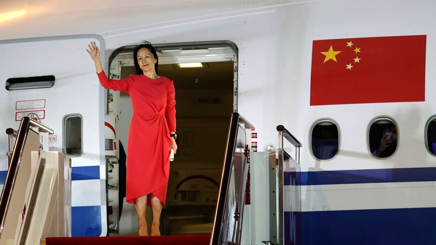 A woman in a red dress waves before descending stairs from an Air China plane.
