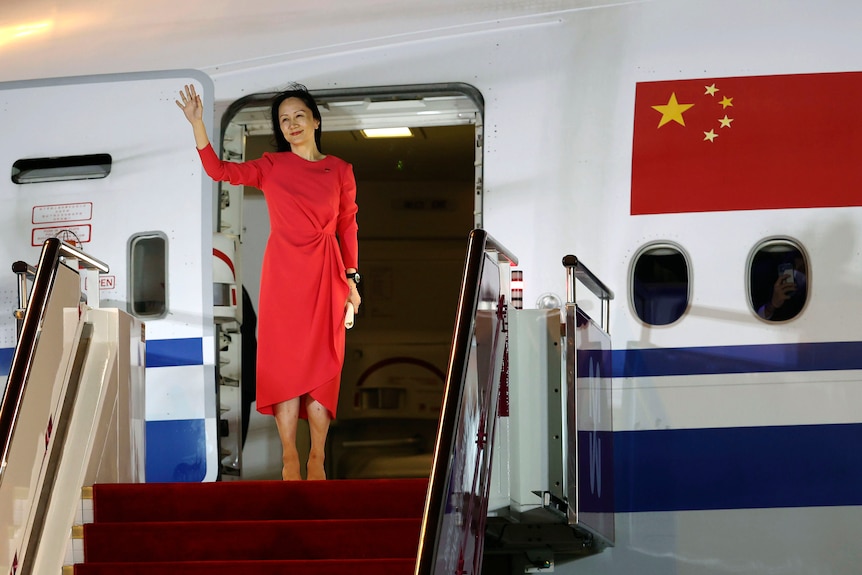 A woman in a red dress waves before descending stairs from an Air China plane.