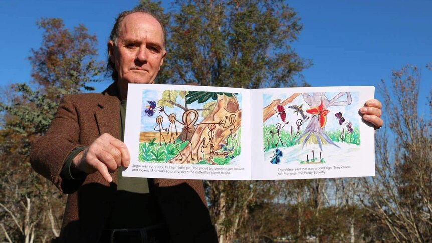 A man holds a children's book showing Indigenous illustrations.
