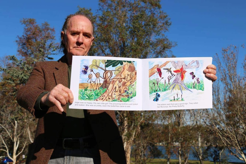 A man holds a children's book showing Indigenous illustrations.