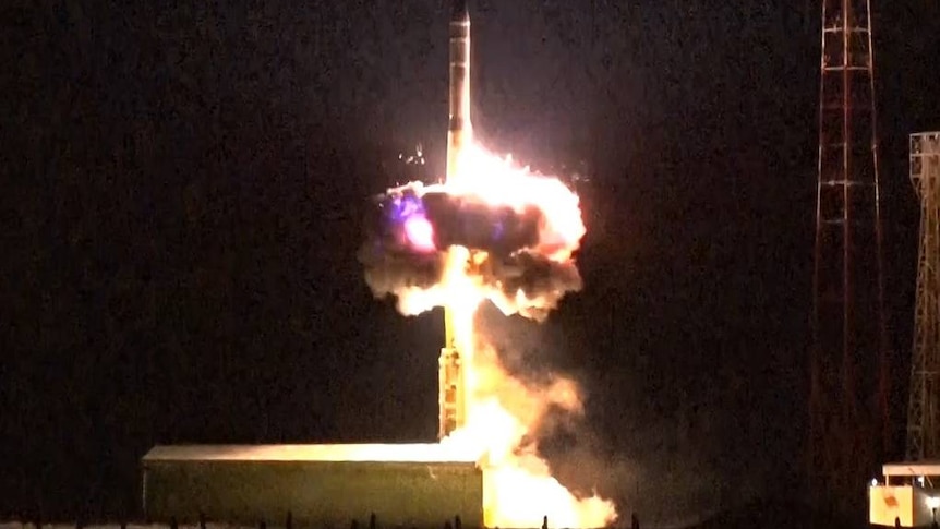 A missile launches at night, leaving a large exhaust blast of flames.