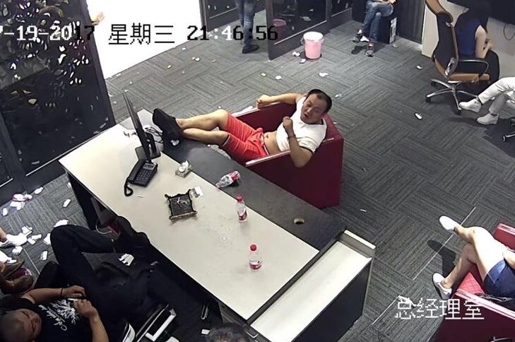 People sit around inside an office building with empty bottles and rubbish lying around.