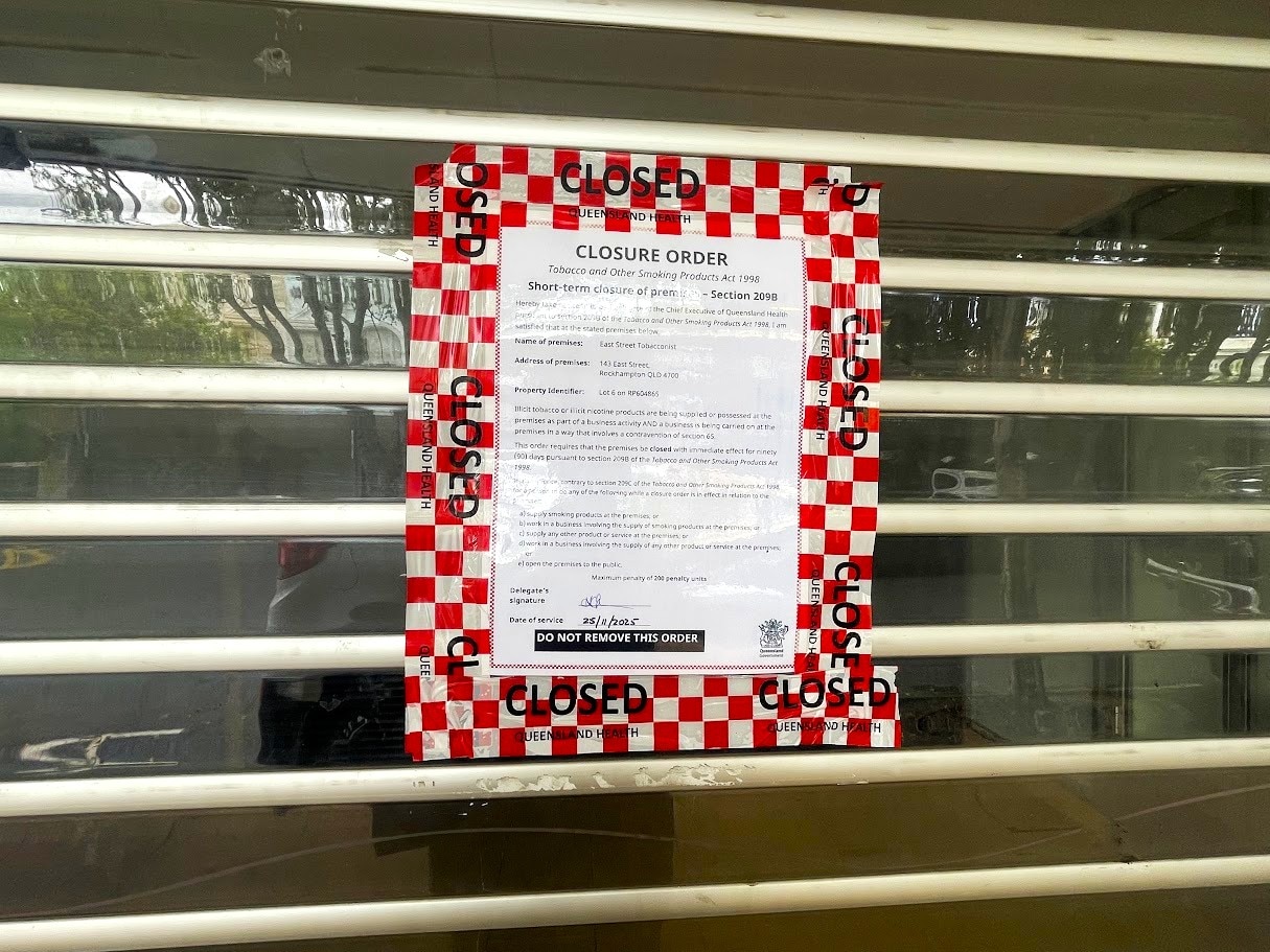 Letrero de papel con texto negro, cinta cerrada a cuadros rojos y blancos, en puerta cerrada con persiana enrollable