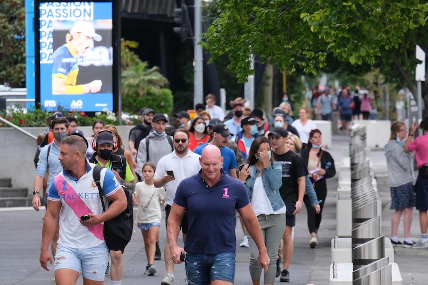 A crowd of men and women walk past a poster of a tennis player with the words passion on it. 