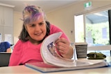 Middle-aged woman with a disability flipping through a drawing booklet while sitting at a table.