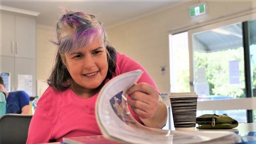 Middle-aged woman with a disability flipping through a drawing booklet while sitting at a table.