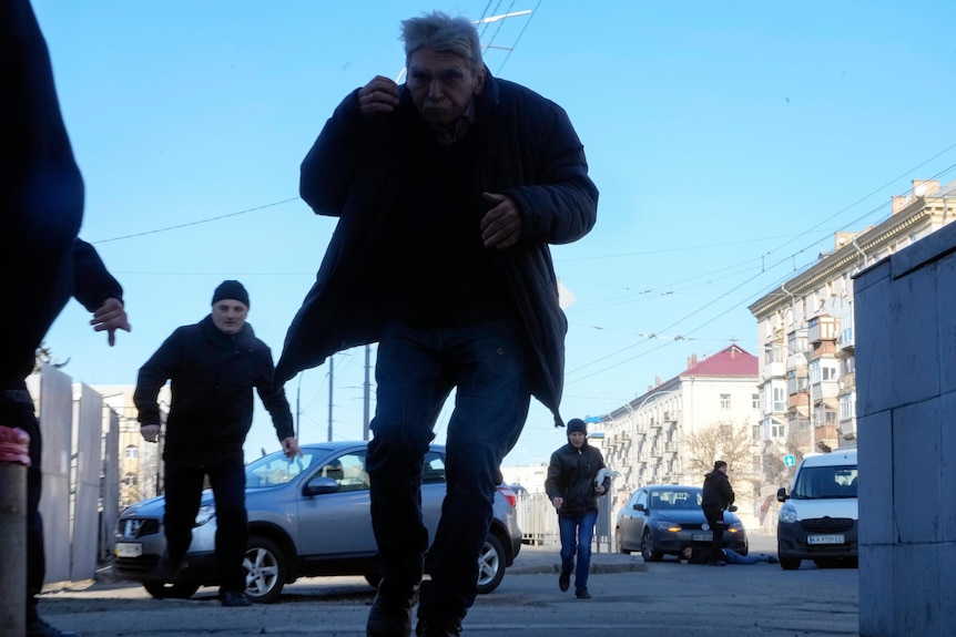 A handful of people who appear to be running from gunfire on a city street