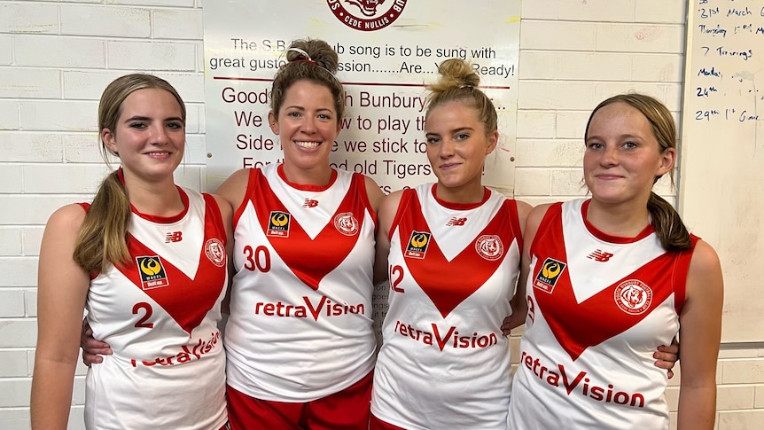 Four women stand next to each other wearing red and white football jumpers.