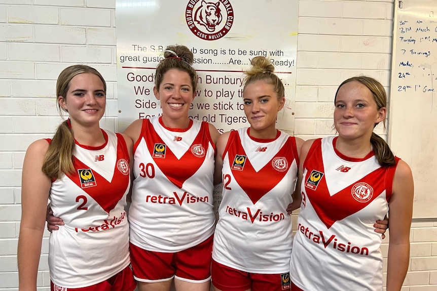 Four women stand next to each other wearing red and white football jumpers