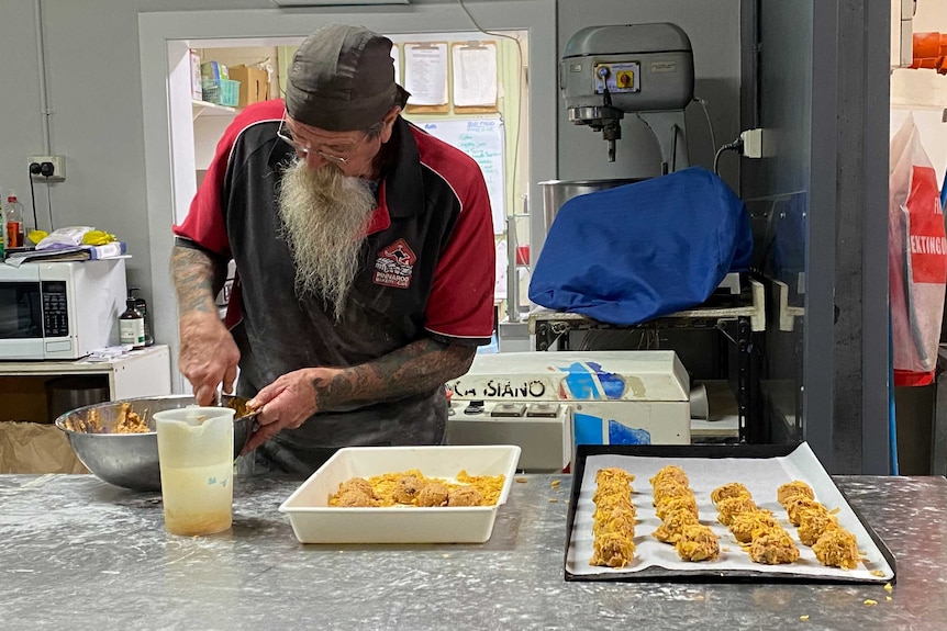 A baker with a long grey beard making cookies on a bench.