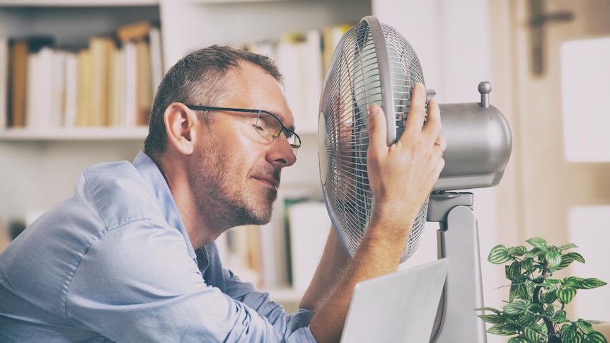 A man holds a desktop fan close to his face.