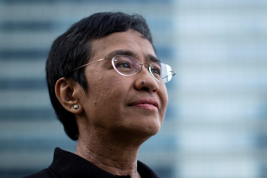 A bespectcled woman with short hair looks off camera as she poses for a headshot.