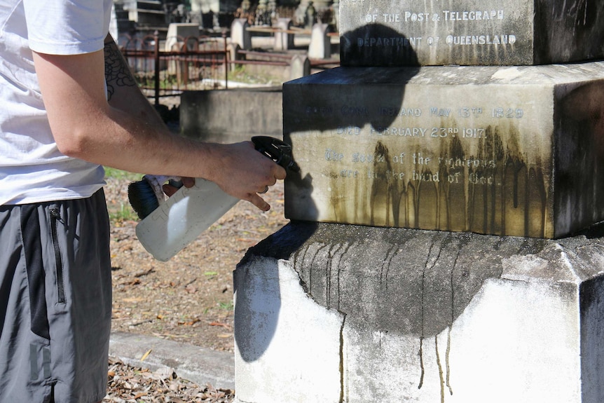 A person sprays grime from a 100 year old grave.
