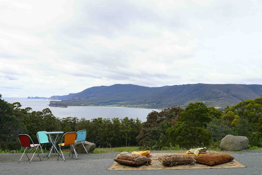 A table and chairs alongside a rug with some pillows. Seating areas at a coffee van that overlooks a beautiful beach