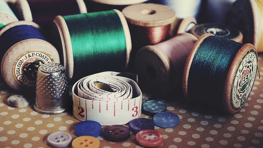 An assortment of coloured threads on wooden spools, a silver thimble, buttons and tailor's measuring tape.