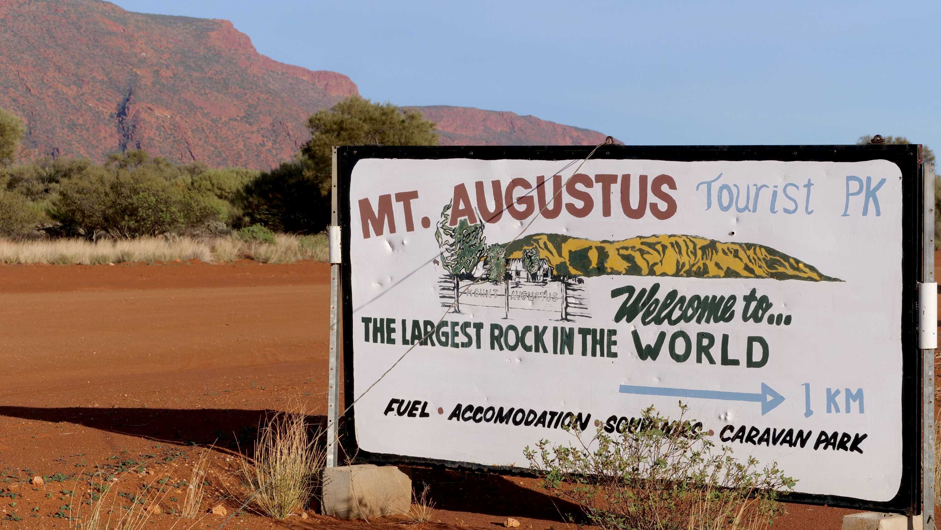 A sign for the Mt Augustus Tourist Park with the big red rock of Mt Augustus in the background.