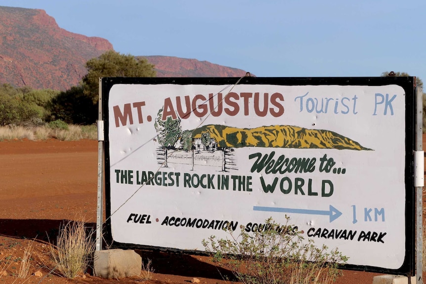 A sign for the Mt Augustus Tourist Park with the big red rock of Mt Augustus in the background.
