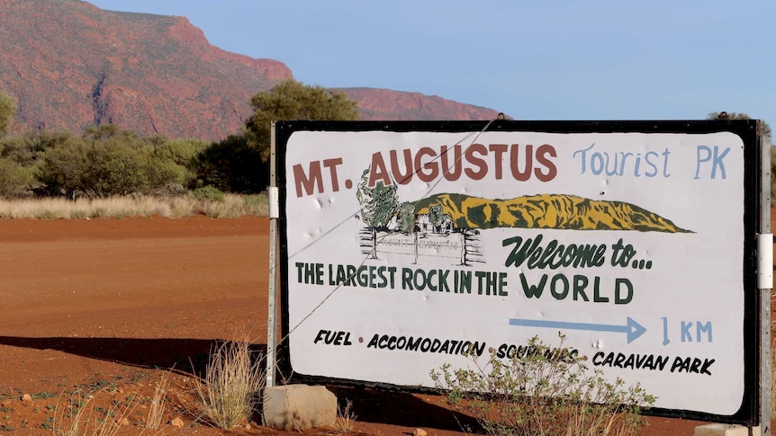 A sign for the Mt Augustus Tourist Park with the big red rock of Mt Augustus in the background.