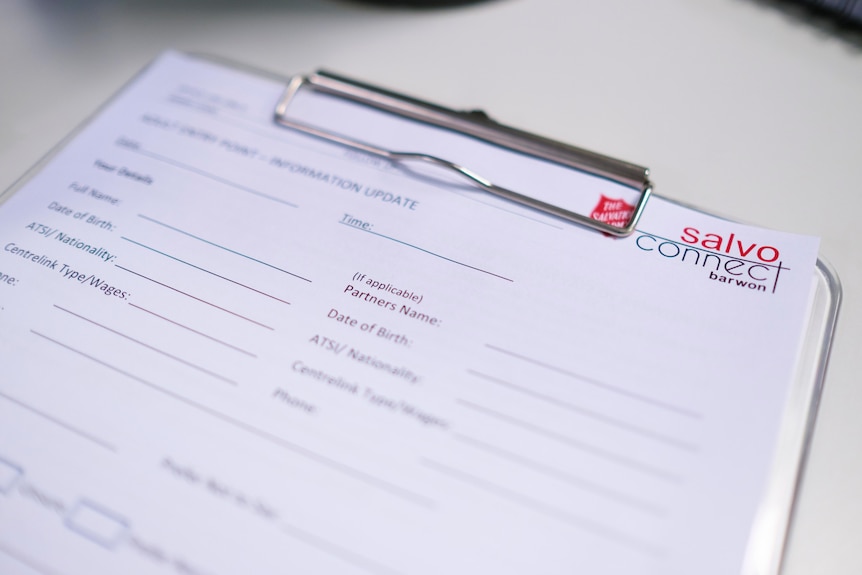 An A4 intake form clipped to a clipboard sits on a desk unfilled with a red Salvation Army logo in the top right hand corner