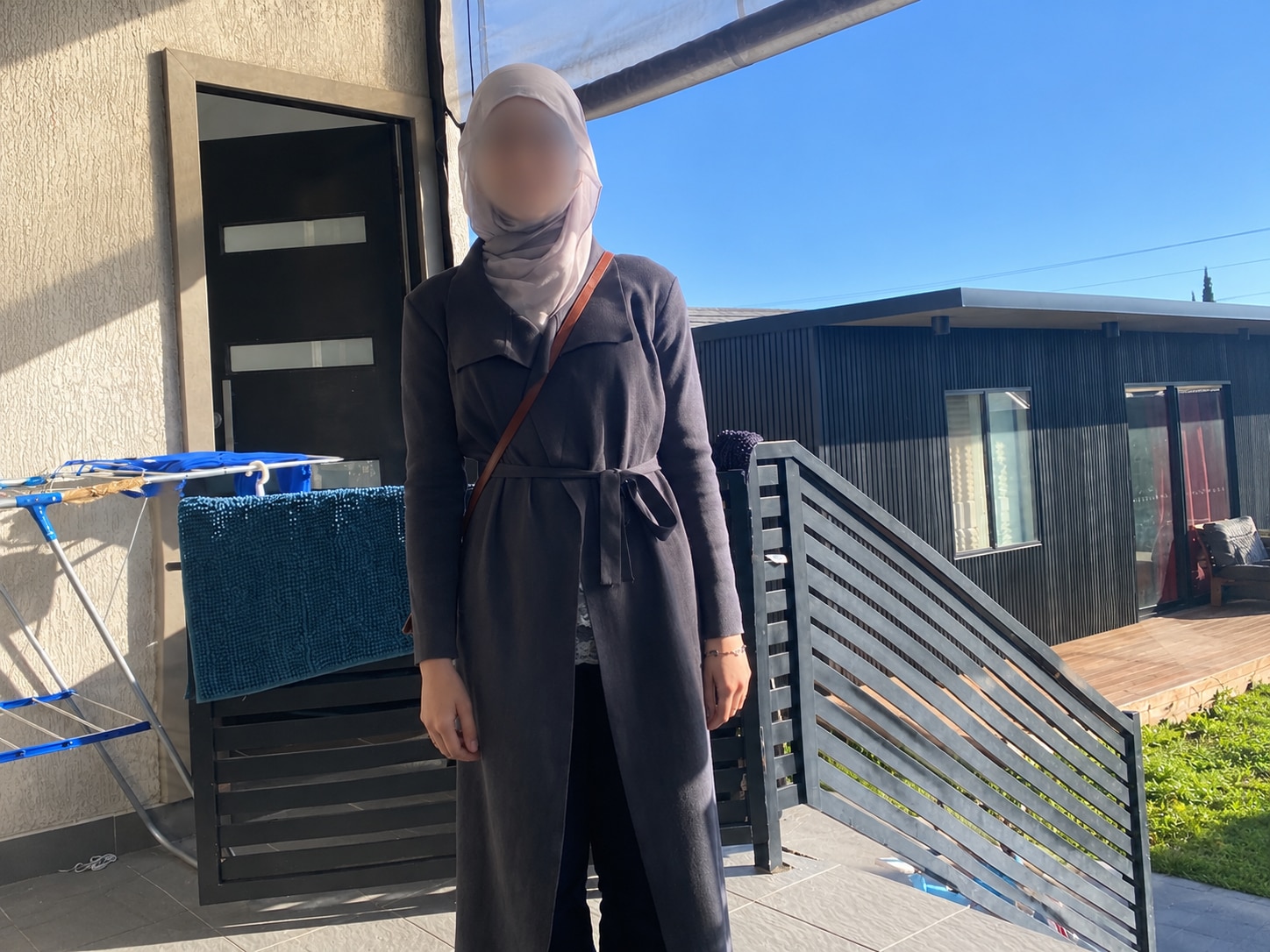 A photo of a woman wearing a dark grey dress and a grey hijab, her face is blurred.