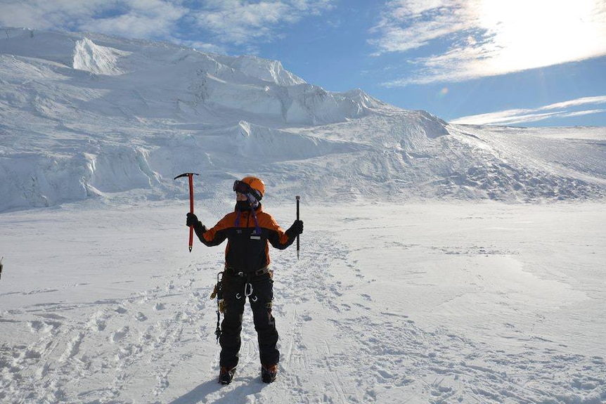 A woman in a snow suit stands in front of polar caps in Antarctica.