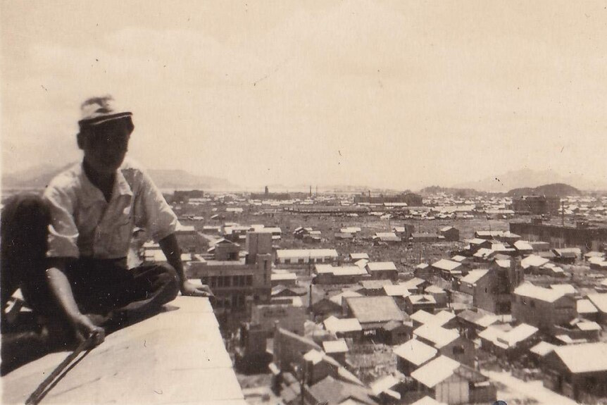 Black and white photo of Man on left, rooftop view out on rubble of city