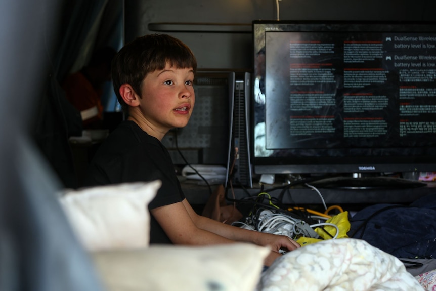 A boy wearing a black t-shirt sits in a tent.