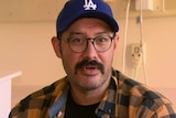 Headshot of a bespectacled man in a baseball cap and plaid shirt.