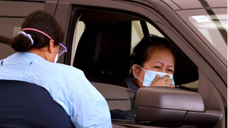 A woman wearing a mask undertakes a drive-thru COVID-19 test.