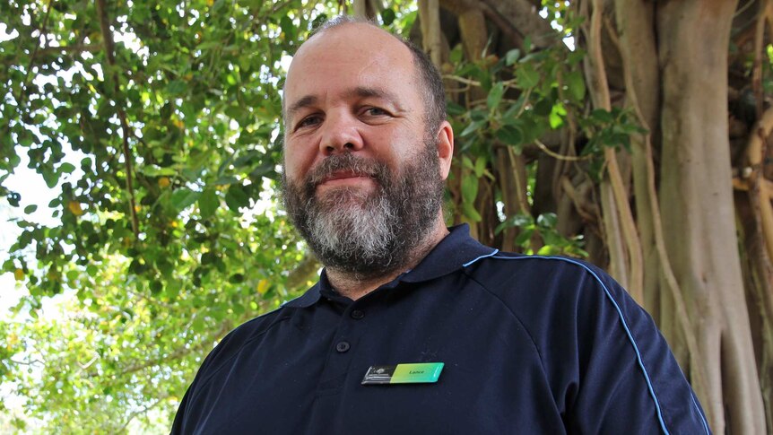 A bearded and friendly-faced fellow, community engagement officer Lance Lofts stands in front of a tree on Townsville's Strand