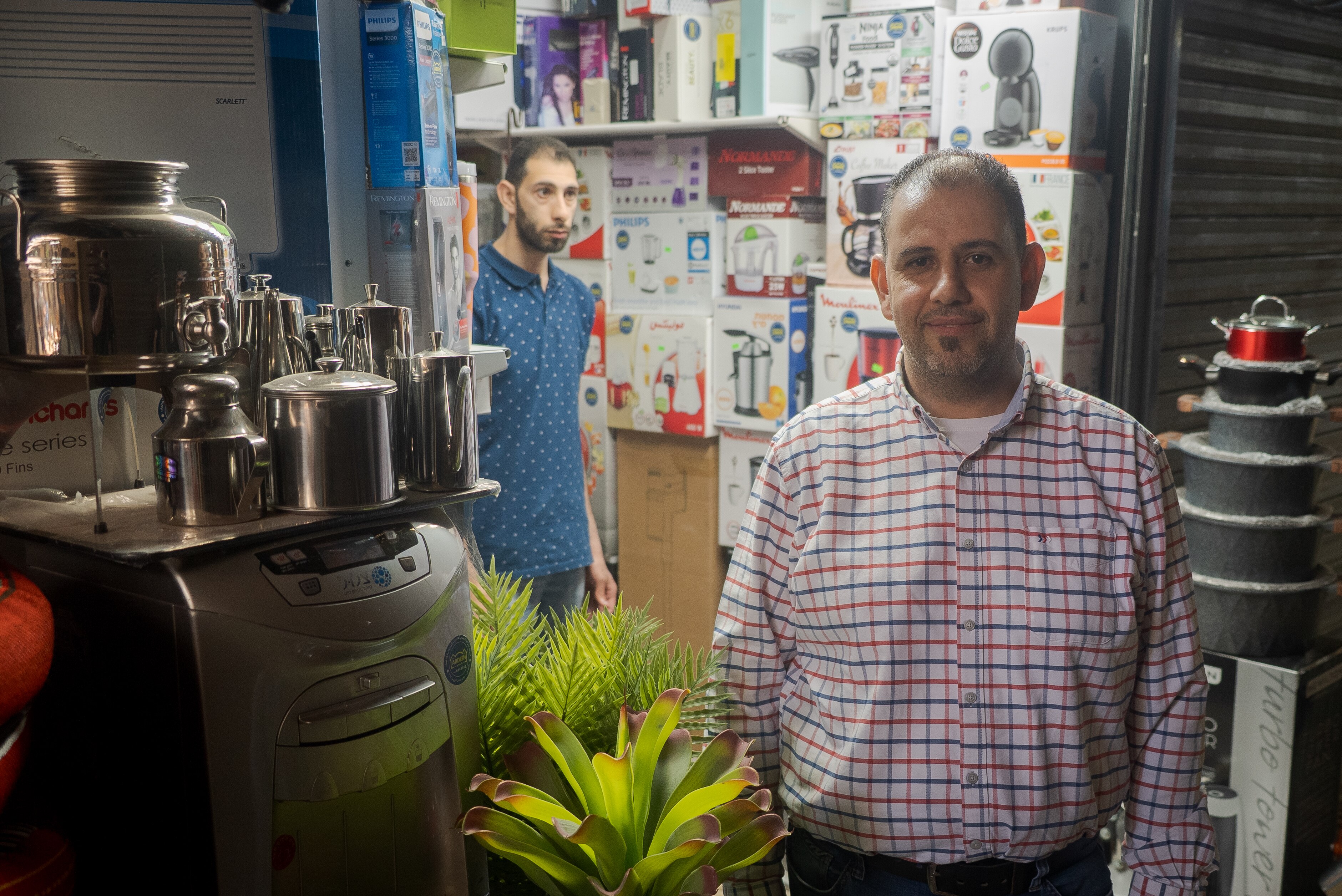 A man in a checked shirt stands in front of a coffee machine