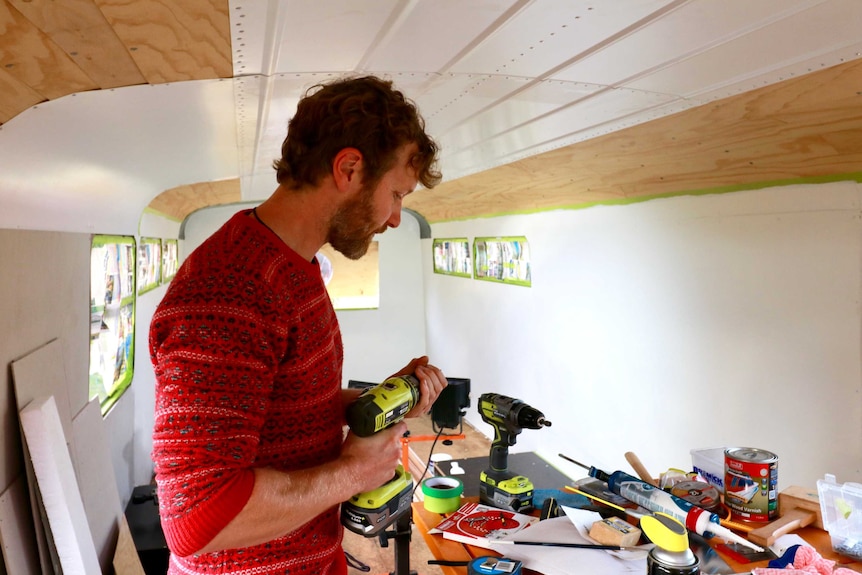 A man inspects a drill inside a bus where restoration is underway.