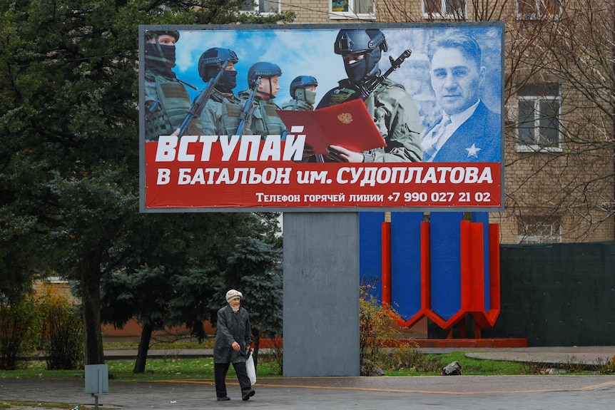 A local resident walks past a board encouraging to join a Russian army battalion in Melitopol, Ukraine.