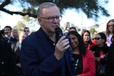 Anthony Albanese holds a microphone while speaking at a community BBQ in Perth