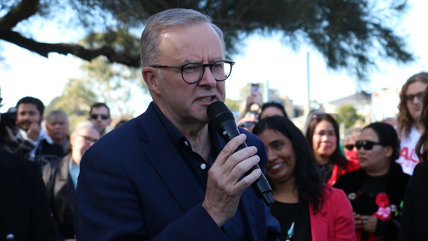 Anthony Albanese holds a microphone while speaking at a community BBQ in Perth