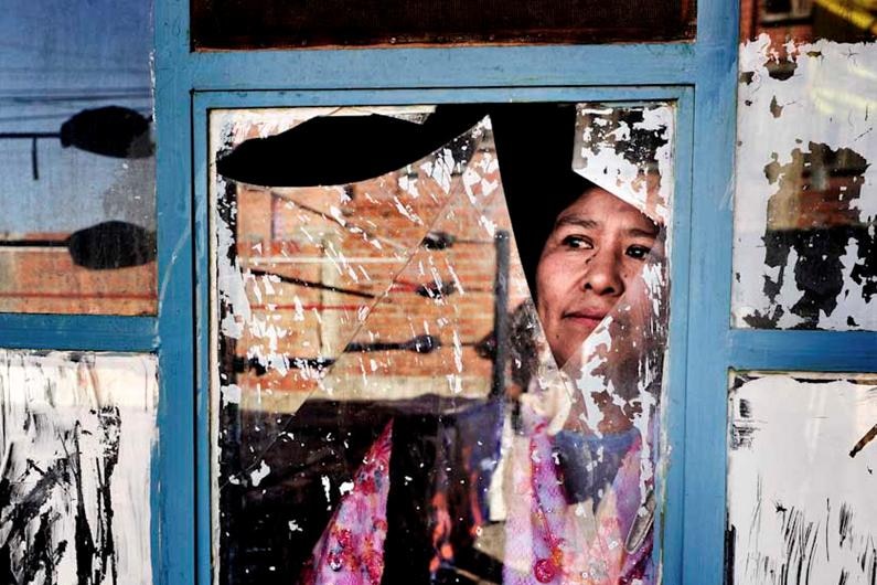 A woman who competes in Bolivian wrestling looks through a broken window.