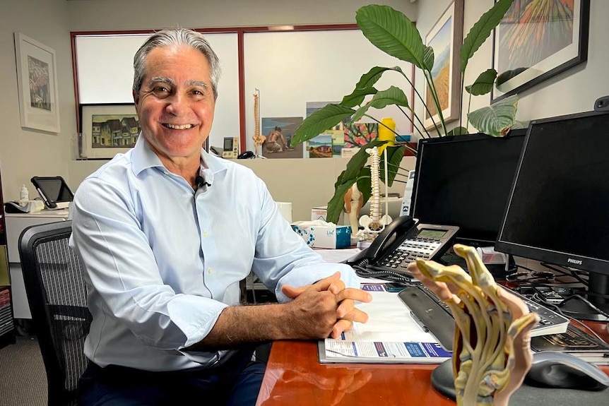 Man smiling at camera in doctor's clinic, with computer and model hand