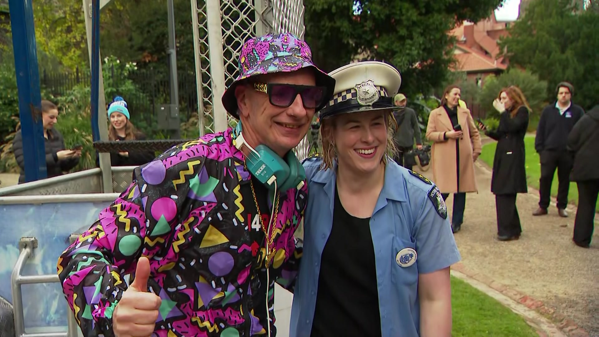 A man in a bright pink, yellow, blue and black outfit stands next to a woman dressed as a police officer.