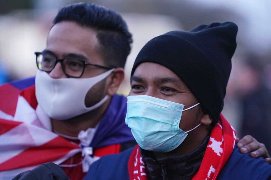 Two men draped in red, white and blue flags wear face masks.