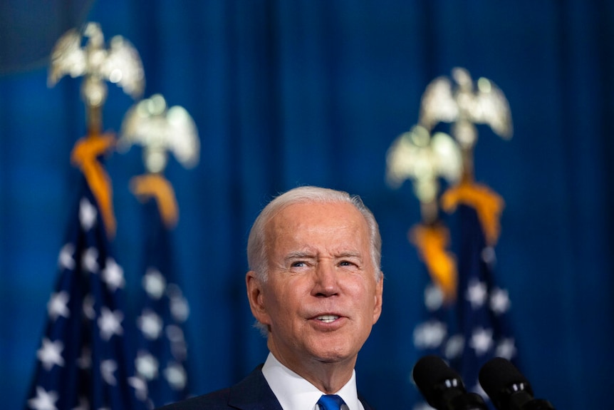Joe Biden gazes upwards as he speaks in front of a blue background. 